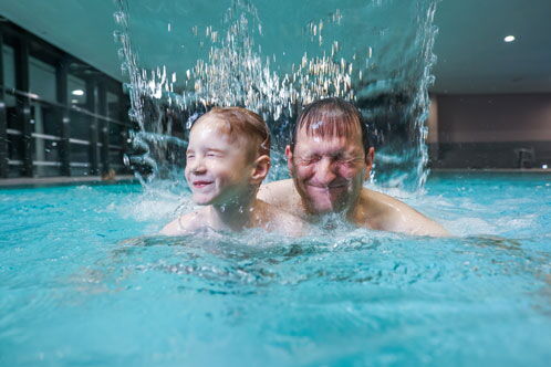 Mann mit seinem kleinen Sohn in einem Hallenbad im Wasser