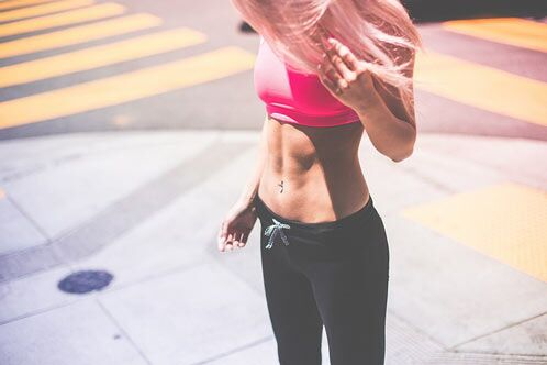 Schlanke, muskulöse Frau mit schwarzer Leggins, bauchfrei mit rosa Top