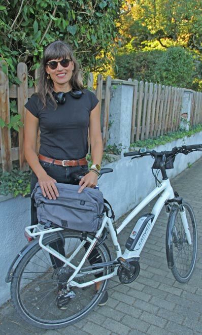 Frau mit grauer Umhängetasche vor einem weißen Fahrrad