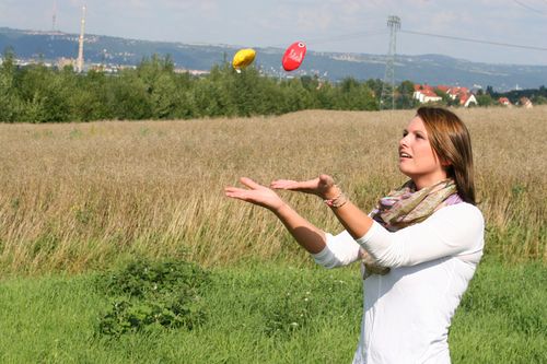 Frau mit weißen Pullover wirft zwei Bälle in die Luft