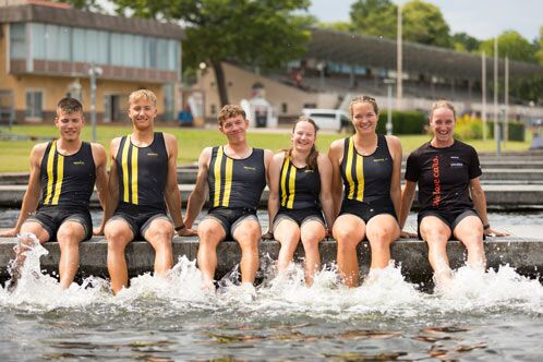 Fünf Ruderer am Ufer sitzend, mit den Beinen im Wasser baumelnd