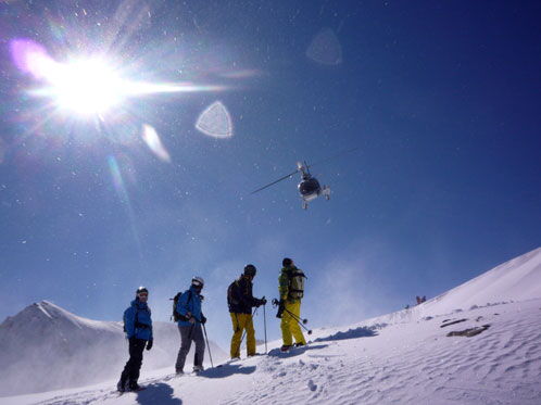 Eine Gruppe von Skifahrern auf einem verschneiten Berg, im Hintergrund ein Hubschrauber.