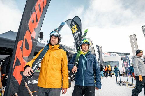 Zwei Skifahrer auf der Piste, die Ski auf den Schultern tragend