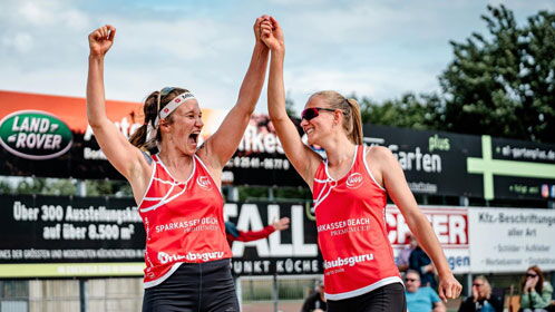 Zwei Beachvolleyballerinnen halten sich an den Händen