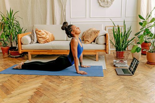 Frau macht Yogapose auf einer blauen Matte im Wohnzimmer