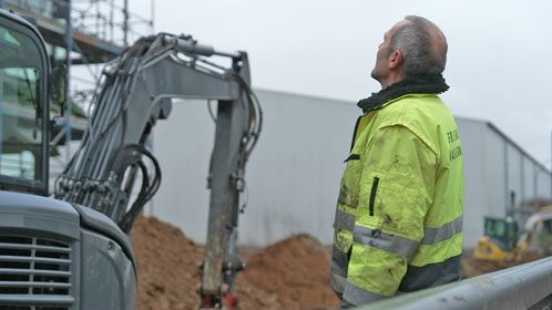 Bauarbeiter mit gelber Weste vor einem Bagger