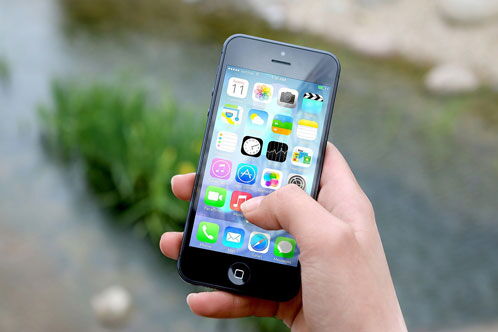 Hand, die ein Smartphone in der Hand hält. Das Display zeigt bunte Symbole.
