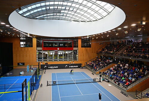 Blick in eine großen Indoortennishalle mit blauem Boden