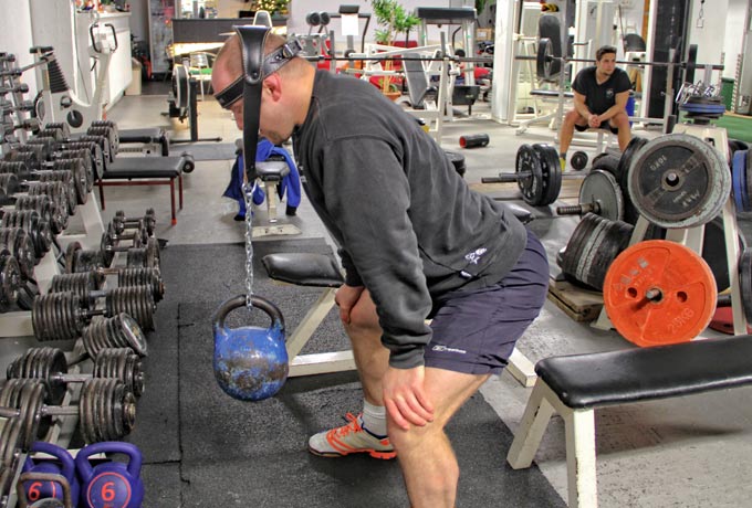 Athletischer Mann mit Kopfband, an dem eine Kettlebell hängt