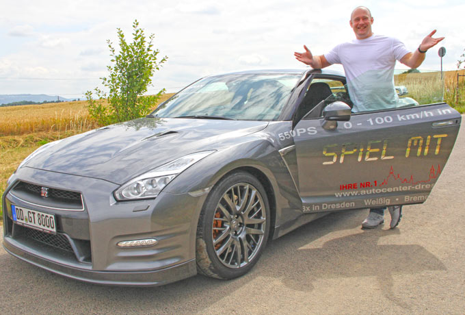 Silberfarbener Nissan GT-R in Seitenansicht, davor steht ein Mann in weißem T-Shirt